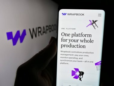 Stuttgart, Almanya - 05-14-2024: Logo önünde ABD 'li yazılım şirketi TakeOne Network Corp' un (Wrapbook) web sayfası ile cep telefonu tutan kişi. Telefon ekranının merkezine odaklan.