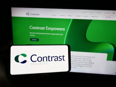 Stuttgart, Almanya - 05-14-2024: İnternet sitesi önünde üzerinde ABD 'li yazılım şirketi Contrast Security Inc.' in logosu bulunan kişi. Telefon ekranına odaklan.