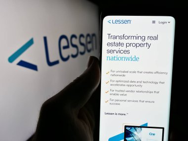 Stuttgart, Almanya - 05-14-2024: ABD 'li emlak hizmetleri pazar yeri şirketi Lessen Inc.' in web sayfası ile logo önünde cep telefonu tutan kişi. Telefon ekranının merkezine odaklan.