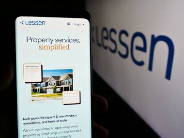 Stuttgart, Almanya - 05-14-2024: ABD 'li emlak hizmetleri pazarlama şirketi Lessen Inc.' in logolu web sayfası ile akıllı telefon sahibi kişi. Telefon ekranının merkezine odaklan.