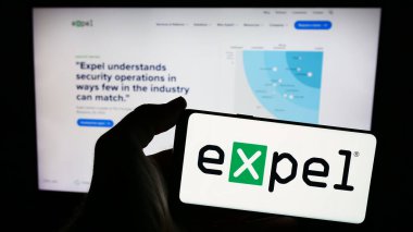 Stuttgart, Germany - 05-14-2024: Person holding smartphone with logo of US cybersecurity company Expel Inc. in front of website. Focus on phone display. clipart