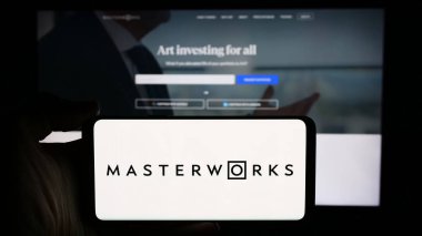 Stuttgart, Germany - 05-16-2024: Person holding cellphone with logo of US art investment company Masterworks LLC in front of business webpage. Focus on phone display. clipart