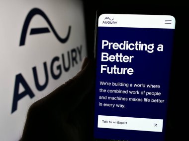 Stuttgart, Almanya - 05-15-2024: İsrailli teknoloji şirketi Augury Ltd. 'nin web sayfası ile birlikte iş logosu önünde cep telefonu tutan kişi. Telefon ekranının merkezine odaklan.