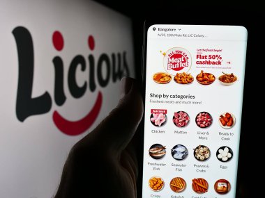 Stuttgart, Almanya - 05-16-2024: Hintli gıda dağıtım şirketi Licious 'un web sitesi ile birlikte iş logosu önünde akıllı telefon tutan kişi. Telefon ekranının merkezine odaklan.
