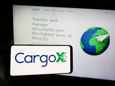 Stuttgart, Germany - 05-15-2024: Person holding smartphone with logo of Slovenian blockchain technology company CargoX Ltd. in front of website. Focus on phone display. clipart