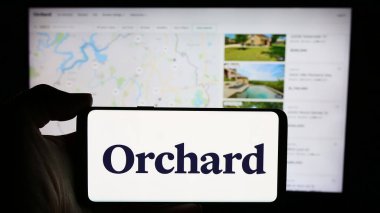 Stuttgart, Almanya - 05-16-2024: İnternet sayfası önünde üzerinde ABD 'li emlak platformu şirketi Orchard Technologies Inc.' in logosu bulunan kişi. Telefon ekranına odaklan.