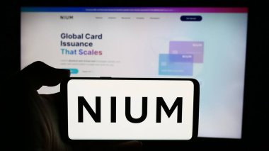 Stuttgart, Almanya - 05-17-2024: Singapur ödeme şirketi Nium Pte 'nin logosuna sahip cep telefonu sahibi kişi. Ltd. İş sayfasının önünde. Telefon ekranına odaklan.