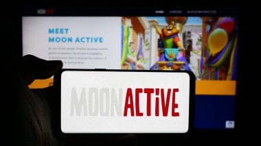 Stuttgart, Almanya - 05-21-2024: İsrailli mobil oyun şirketi Moon Active Ltd. 'nin logosuyla cep telefonu tutan kişi iş sayfasının önünde. Telefon ekranına odaklan.