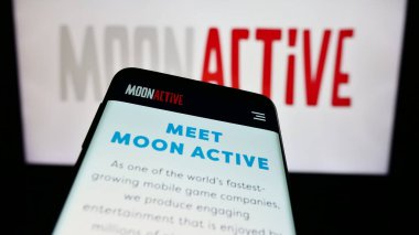 Stuttgart, Almanya - 05-21-2024: İsrailli mobil oyun şirketi Moon Active Ltd. 'nin web sitesi ile birlikte ticaret logosu önünde akıllı telefon. Telefon ekranının sol üst kısmına odaklan.