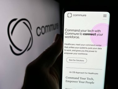 Stuttgart, Almanya - 05-21-2024: ABD 'li sağlık yazılım şirketi Commure Inc.' in web sitesi ile iş logosu önünde akıllı telefon tutan kişi. Telefon ekranının merkezine odaklan.