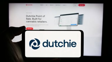 Stuttgart, Almanya - 05-21-2024: Üzerinde ABD 'li esrar şirketi Courier Plus Inc. (Dutchie)' nin logosu bulunan cep telefonu sahibi kişi iş sayfası önünde. Telefon ekranına odaklan.