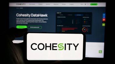 Stuttgart, Almanya - 05-21-2024: ABD 'li veri yönetim şirketi Cohesity Inc.' in logosuyla cep telefonu sahibi kişi iş sayfasının önünde. Telefon ekranına odaklan.