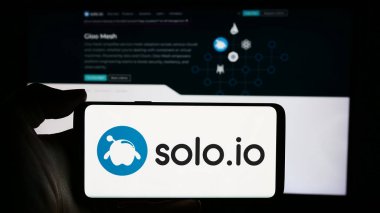 Stuttgart, Germany - 05-15-2024: Person holding cellphone with logo of US networking platform company Solo.io Inc. in front of business webpage. Focus on phone display. clipart