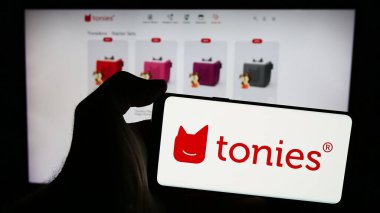 Stuttgart, Almanya - 05-22-2024: Alman oyuncak perakende şirketi Tonies SE 'nin (Toniebox) logosuna sahip cep telefonu sahibi kişi iş sayfasının önünde. Telefon ekranına odaklan.