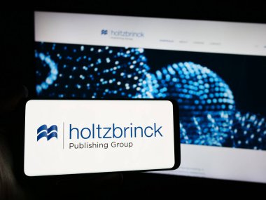 Stuttgart, Almanya - 05-22-2024: Alman medya şirketi Holtzbrinck Publishing Group 'un logosuna sahip akıllı telefon sahibi kişi web sitesi önünde. Telefon ekranına odaklan.