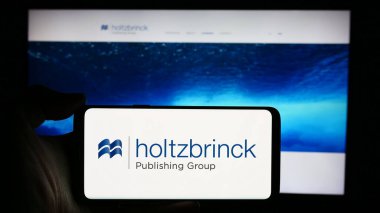 Stuttgart, Almanya - 05-22-2024: Alman medya şirketi Holtzbrinck Publishing Group 'un logosuyla cep telefonu sahibi kişi iş sayfası önünde. Telefon ekranına odaklan.