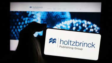 Stuttgart, Almanya - 05-22-2024: Alman medya şirketi Holtzbrinck Publishing Group 'un logosuyla cep telefonu sahibi kişi iş sayfası önünde. Telefon ekranına odaklan.