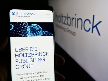 Stuttgart, Almanya - 05-22-2024: Alman medya şirketi Holtzbrinck Publishing Group 'un internet sayfası ile logo önünde cep telefonu tutan kişi. Telefon ekranının merkezine odaklan.