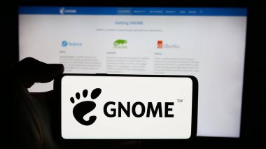 Stuttgart, Almanya - 05-22-2024: İnternet sayfası önünde açık kaynak GNU Ağ Nesne Ortamı (GNOME) logosu bulunan kişi. Telefon ekranına odaklan.