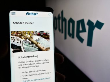 Stuttgart, Almanya - 05-22-2024: Alman sigorta şirketi Gothaer Versicherungsbank VVaG 'ın logolu web sayfası ile cep telefonu tutan kişi. Telefon ekranının merkezlerine odaklan.