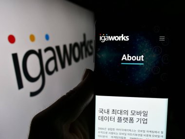 Stuttgart, Almanya - 05-15-2024: Güney Koreli dijital pazarlama şirketi IGAWorks 'ün logo önündeki web sayfası ile cep telefonu tutan kişi. Telefon ekranının merkezine odaklan.