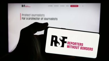 Stuttgart, Germany - 05-23-2024: Person holding mobile phone with logo of international organisation Reporters Without Borders in front of web page. Focus on phone display. clipart