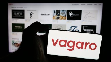 Stuttgart, Almanya - 05-15-2024: İş sayfasının önünde ABD 'li sağlıklı pazar yeri şirketi Vagaro Inc.' nin logosuna sahip cep telefonu sahibi kişi. Telefon ekranına odaklan.