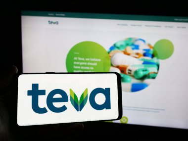 Stuttgart, Almanya - 05-23-2024: İsrailli Teva Pharmaceutical Industries Ltd. 'nin logosuna sahip akıllı telefon sahibi kişi web sitesi önünde. Telefon ekranına odaklan.