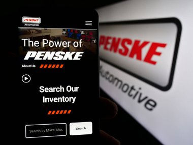 Stuttgart, Almanya - 05-23-2024: ABD 'li otomotiv şirketi Penske Automotive Group Inc.' in web sayfası ile logo önünde akıllı telefon bulunduran kişi. Telefon ekranının merkezine odaklan.