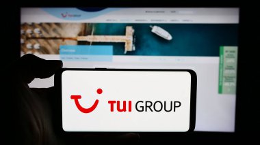 Stuttgart, Almanya - 05-23-2024: Alman seyahat ve turizm şirketi TUI AG 'nin logosuna sahip cep telefonu sahibi kişi iş sayfası önünde. Telefon ekranına odaklan.