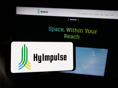 Stuttgart, Germany - 05-24-2024: Person holding mobile phone with logo of German aerospace company HyImpulse Technologies GmbH in front of web page. Focus on phone display. clipart