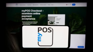 Stuttgart, Germany - 05-27-2024: Person holding cellphone with logo of British payment technology company myPOS World Ltd. in front of business webpage. Focus on phone display. clipart