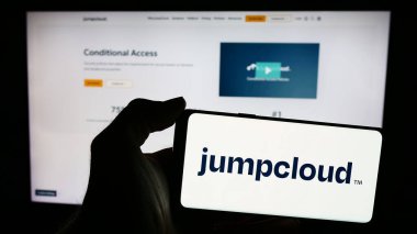 Stuttgart, Germany - 05-27-2024: Person holding mobile phone with logo of American cloud software company JumpCloud Inc. in front of business web page. Focus on phone display. clipart