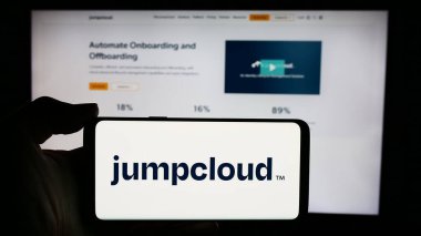 Stuttgart, Germany - 05-27-2024: Person holding cellphone with logo of US cloud software company JumpCloud Inc. in front of business webpage. Focus on phone display. clipart