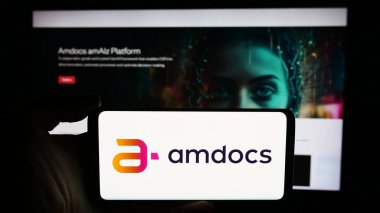 Stuttgart, Germany - 05-27-2024: Person holding cellphone with logo of Israeli telecom technology company Amdocs Limited in front of business webpage. Focus on phone display. clipart