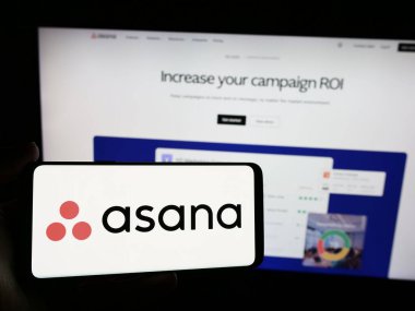 Stuttgart, Almanya - 05-27-2024: İnternet sitesi önünde üzerinde ABD 'li iş yönetimi yazılım şirketi Asana Inc.' in logosu bulunan akıllı telefon sahibi kişi. Telefon ekranına odaklan.