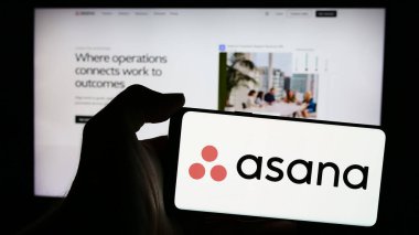 Stuttgart, Almanya - 05-27-2024: İnternet sayfası önünde üzerinde Amerikan iş yönetimi yazılım şirketi Asana Inc. 'in logosu bulunan cep telefonu sahibi kişi. Telefon ekranına odaklan.