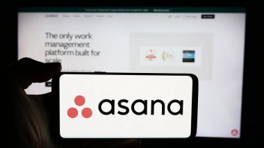 Stuttgart, Almanya - 05-27-2024: ABD 'li iş yönetimi yazılım şirketi Asana Inc.' in logosuyla cep telefonu sahibi kişi iş sayfasının önünde. Telefon ekranına odaklan.