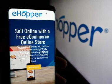 Stuttgart, Almanya - 05-27-2024: ABD satış sistemleri şirketi eHopper Services Inc. 'nin logolu web sayfası ile cep telefonu tutan kişi. Telefon ekranının merkezine odaklan.
