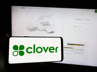 Stuttgart, Almanya - 05-27-2024: İnternet sayfasının önünde üzerinde Amerikan satış platformu şirketi Clover Network Inc. 'in logosu bulunan cep telefonu sahibi kişi. Telefon ekranına odaklan.