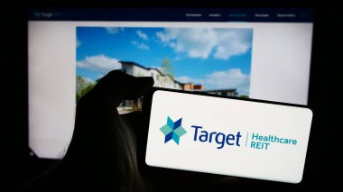 Stuttgart, Almanya - 05-29-2024: İngiliz emlak şirketi Target Healthcare REIT 'in logosuyla cep telefonu sahibi kişi iş sayfası önünde. Telefon ekranına odaklan.