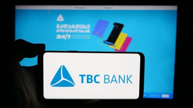 Stuttgart, Germany - 05-29-2024: Person holding cellphone with logo of Georgian financial services company TBC Bank Group plc in front of webpage. Focus on phone display. clipart