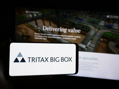 Stuttgart, Almanya - 05-29-2024: İngiliz emlak şirketi Tritax Big Box REIT plc 'in logosuna sahip akıllı telefon sahibi kişi web sitesinin önünde. Telefon ekranına odaklan.