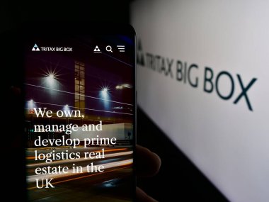 Stuttgart, Almanya - 05-29-2024: İngiliz emlak şirketi Tritax Big Box REIT plc 'in web sayfası ile logo önünde cep telefonu tutan kişi. Telefon ekranının merkezine odaklan.