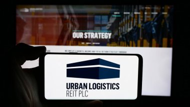 Stuttgart, Almanya - 05-30-2024: İngiliz emlak şirketi Urban Logistics REIT plc 'in logosuna sahip akıllı telefon sahibi kişi web sitesi önünde. Telefon ekranına odaklan.