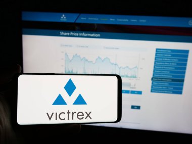 Stuttgart, Almanya - 05-30-2024: İngiliz polimer yapım şirketi Victrex plc 'in logosuna sahip cep telefonu sahibi kişi iş sayfasının önünde. Telefon ekranına odaklan.