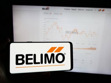 Stuttgart, Almanya - 05-31-2024: İsviçreli kontrol sistemleri şirketi Belimo Holding AG 'nin logosunun bulunduğu cep telefonu sahibi kişi iş sayfasının önünde. Telefon ekranına odaklan.