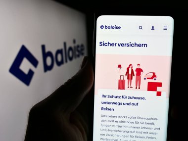 Stuttgart, Almanya - 05-31-2024: İsviçreli sigorta şirketi Baloise Holding AG 'nin internet sayfası ile iş logosu önünde cep telefonu tutan kişi. Telefon ekranının merkezine odaklan.