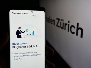 Stuttgart, Almanya - 05-31-2024: İsviçreli havaalanı operatörü Flughafen Zürih AG (FZAG) 'nin logolu web sayfası ile cep telefonu tutan kişi. Telefon ekranının merkezine odaklan.