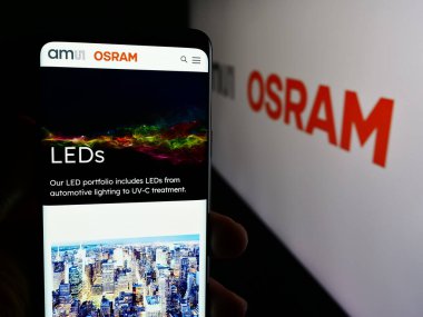 Stuttgart, Almanya - 05-31-2024: Avusturyalı elektronik şirketi OSRAM AG 'ın web sayfası ile cep telefonu tutan kişi iş logosu önünde. Telefon ekranının merkezine odaklan.